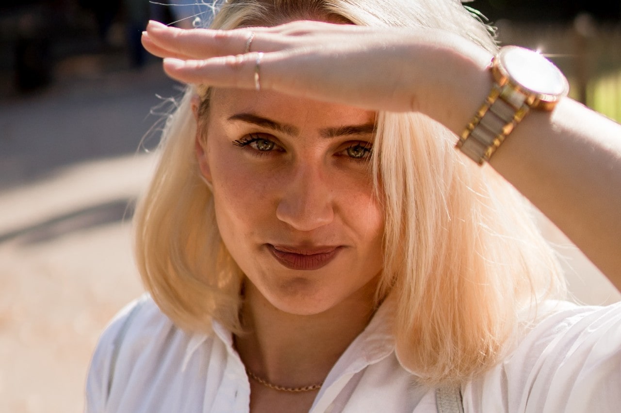 A close-up of a woman wearing a mixed metal watch shielding her eyes from the sun.