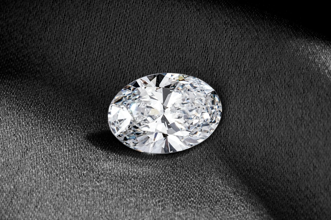 A single oval-cut diamond displayed on a dark fabric background.