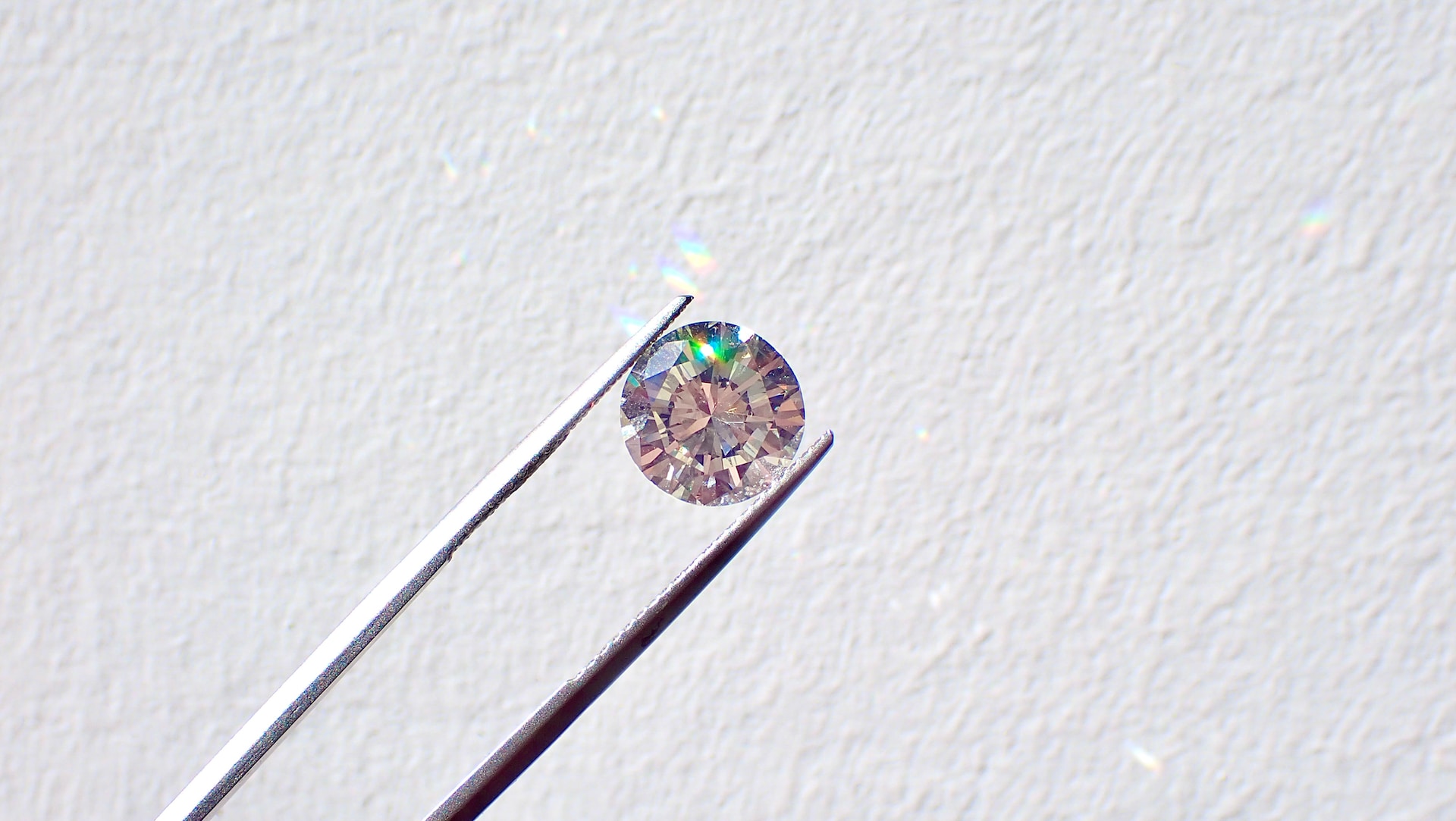 A close-up of tweezers holding a small round-cut diamond.