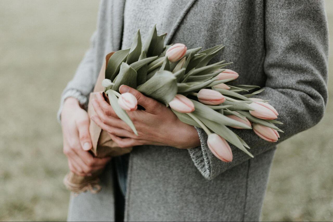 A mother wearing a gray cardigan holds a bouquet of tulips.