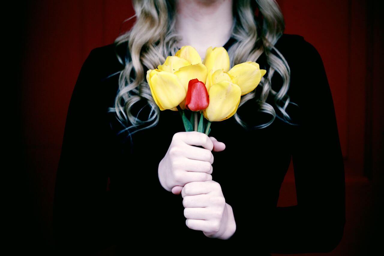 A woman in a black top holds a bundle of yellow and red flowers.