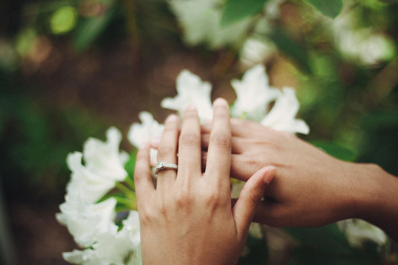 Two hands hovering over a bouquet. The left showcases a gorgeous engagement ring