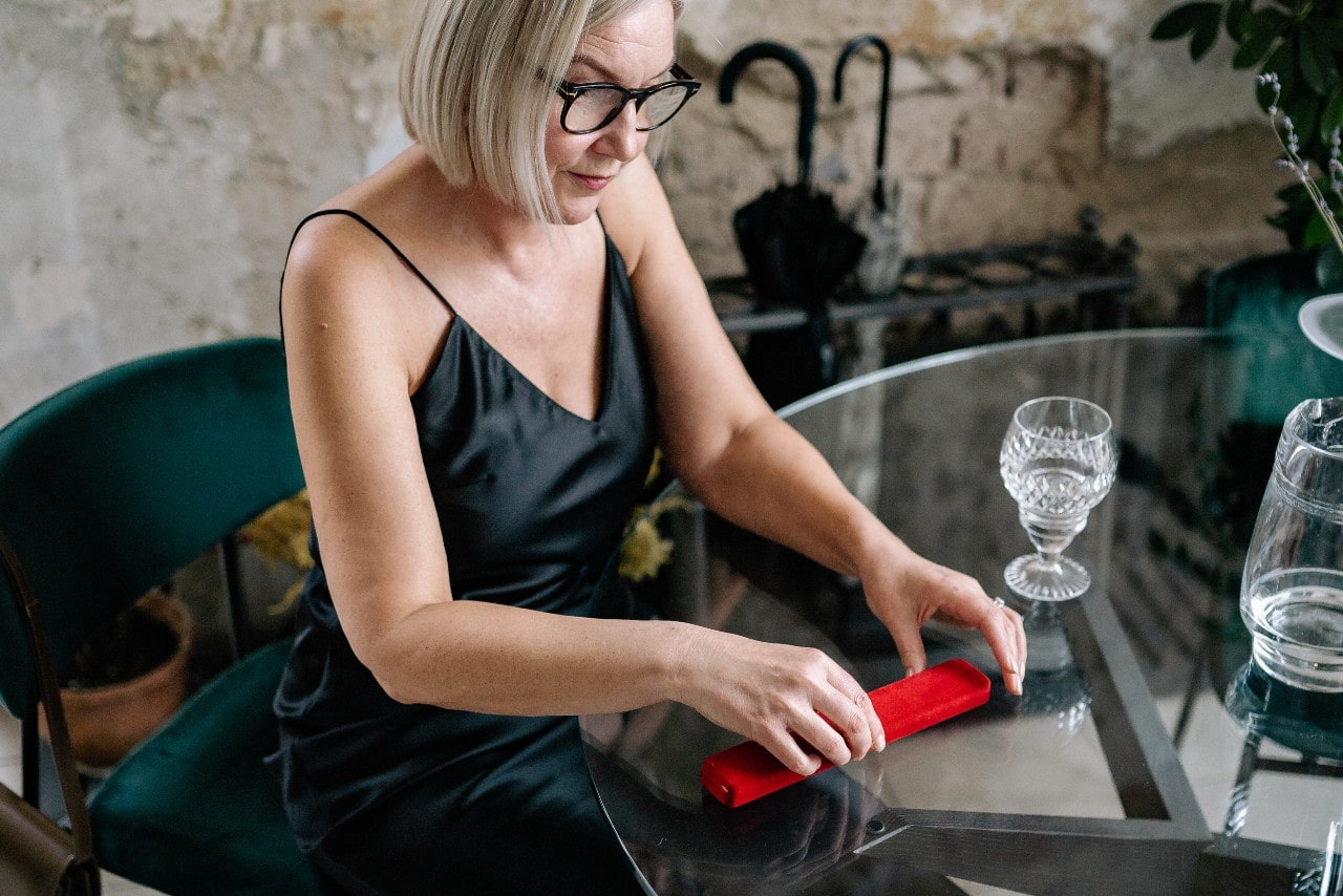 A mom about open a new necklace in a long, red jewelry box at her dining room table