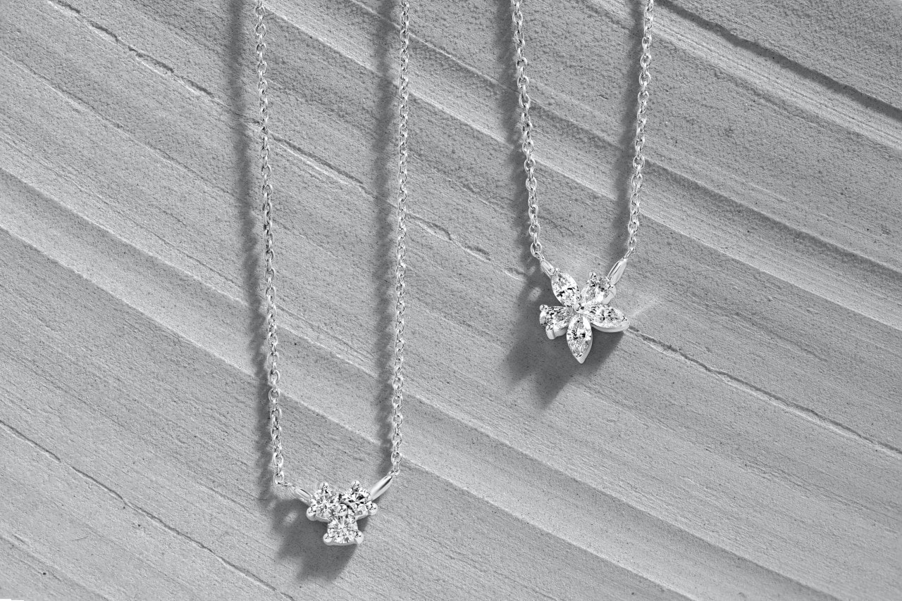 Two white gold diamond pendants sit on a gray wooden surface