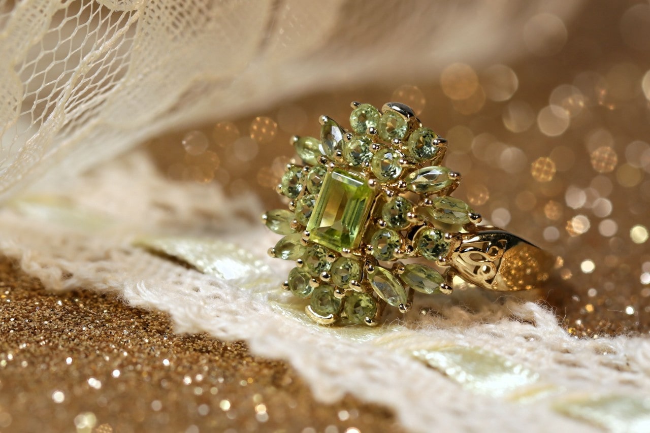 An elaborately designed peridot fashion ring on a glittery surface