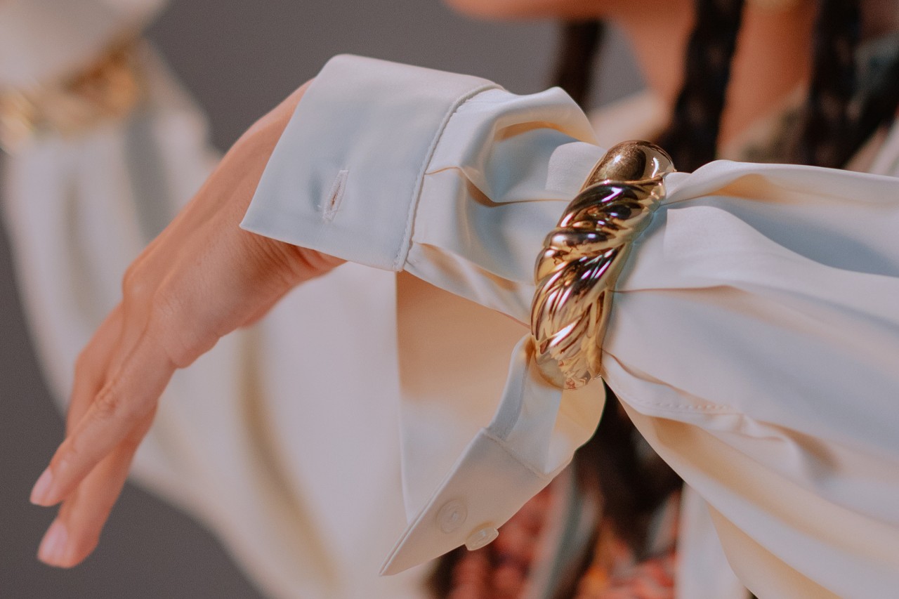 A woman’s arm clad in a white sleeve and a chunky gold cuff bracelet