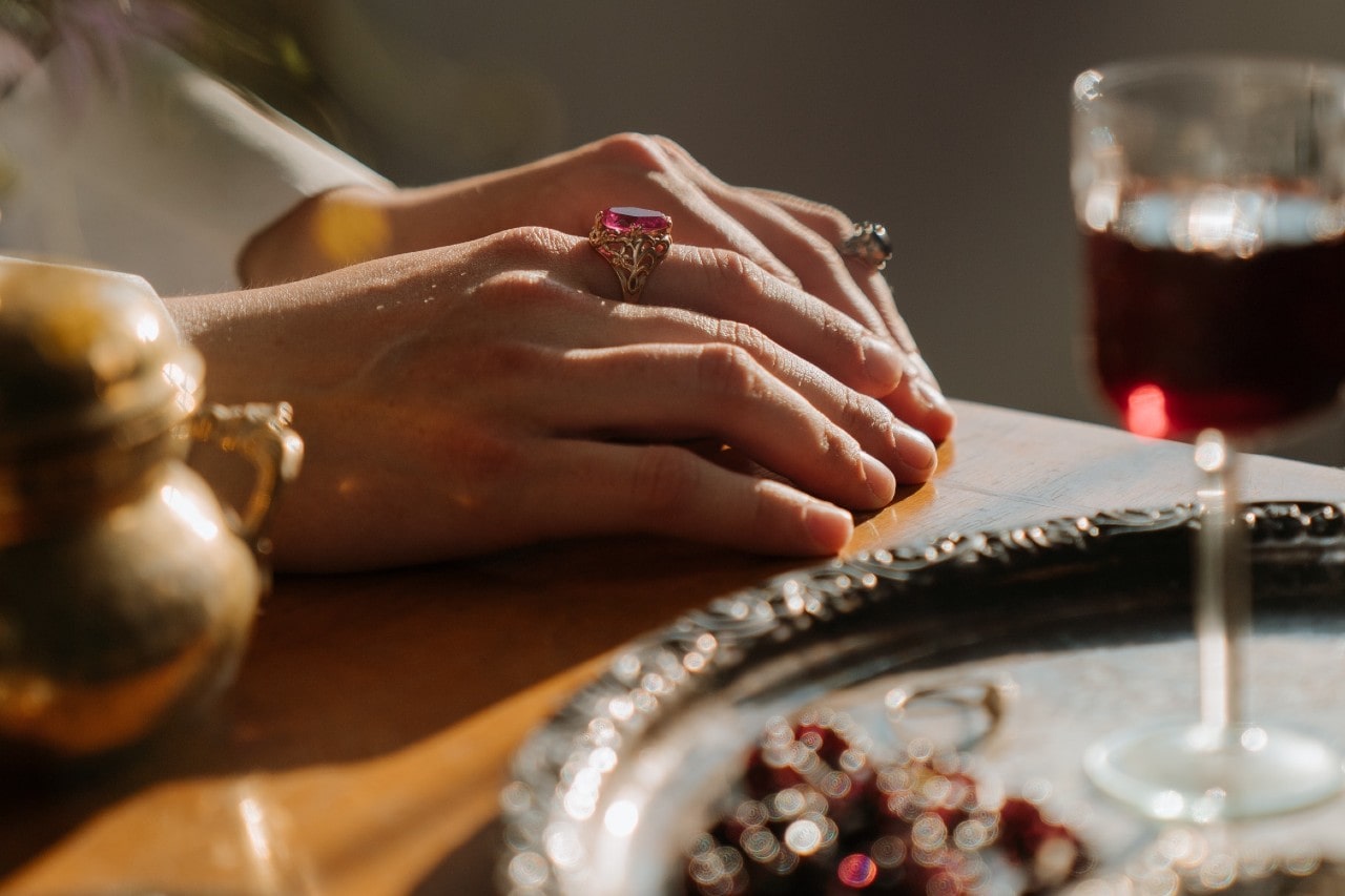 a woman’s hand lying on a table set with vintage items, wearing multiple gemstone rings