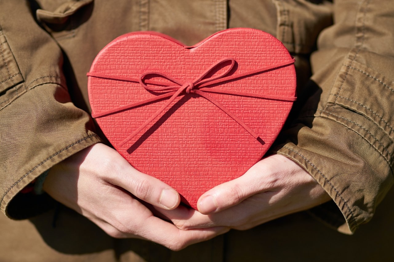 a woman in a brown jacket holding a red, heart-shaped box