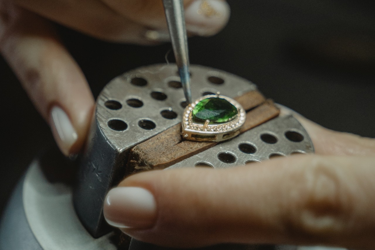 a jeweler creating a green pear shape pendant with a diamond halo