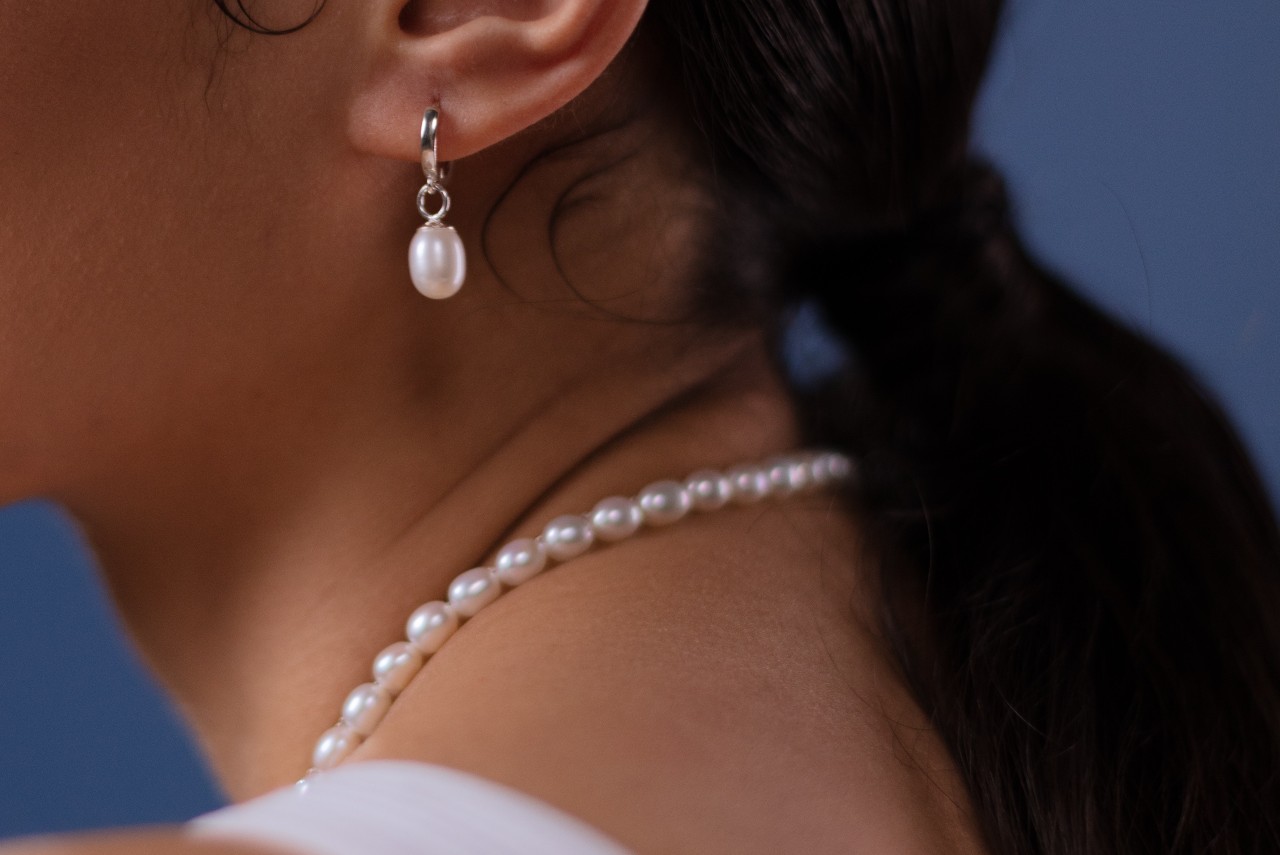 A close-up image of a woman’s neck adorned with a pearl necklace and a matching earring in her ear