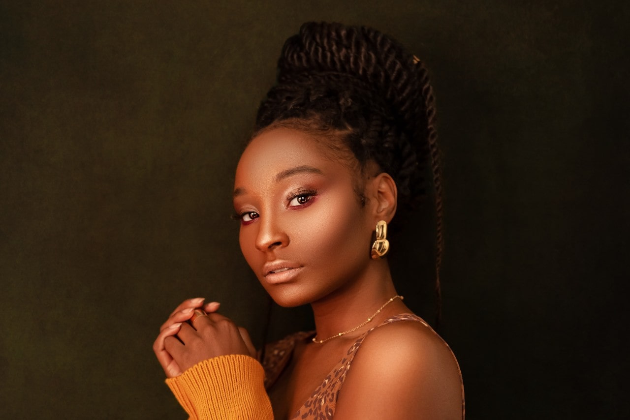 A woman looking into the camera, wearing large gold earrings and a dainty gold necklace.