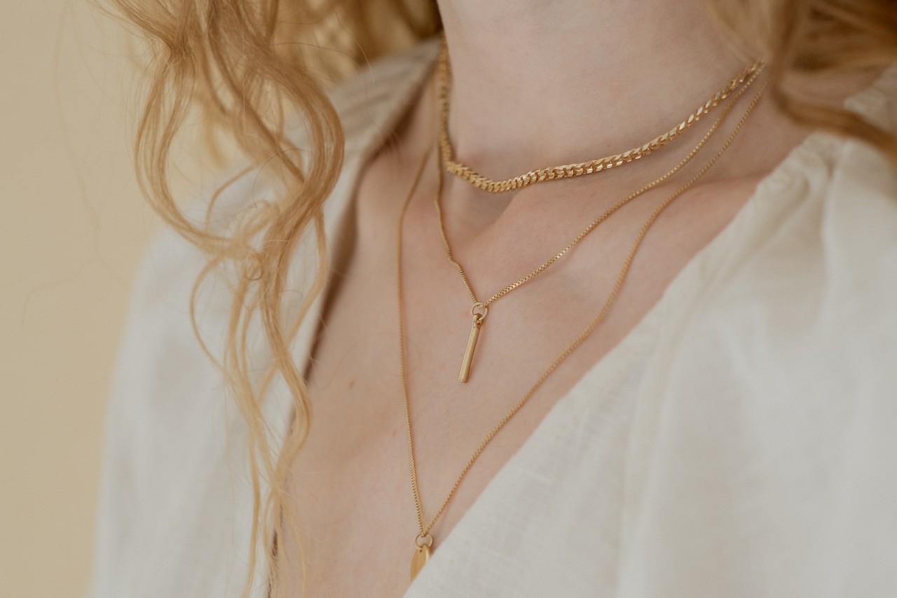 A close-up image of a woman’s neckline adorned with three matching gold necklaces.