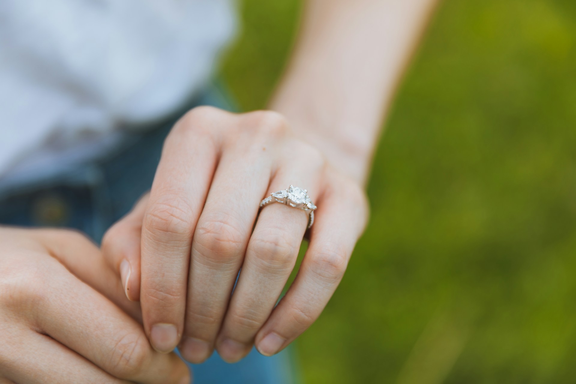A woman wearing a white gold three stone engagement ring in a grassy field. A woman wearing a white gold three stone engagement ring in a grassy field.