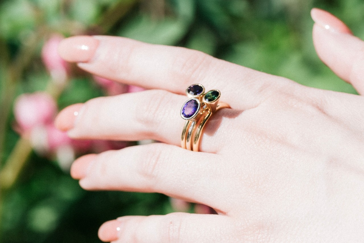an outstretched woman’s hand wearing three stacked gemstone rings