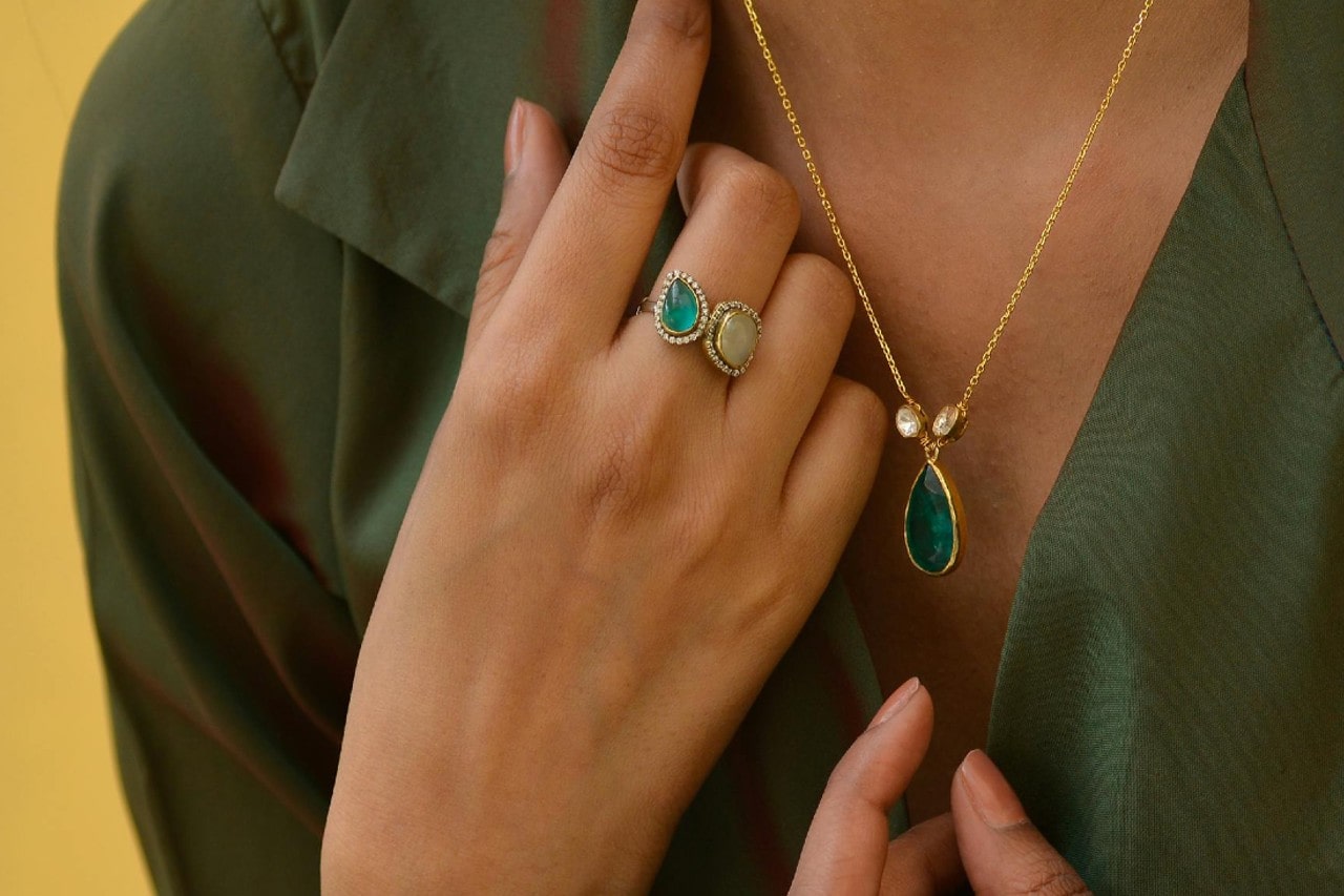 a woman wearing a green gemstone pendant necklace and a toi et moi fashion ring