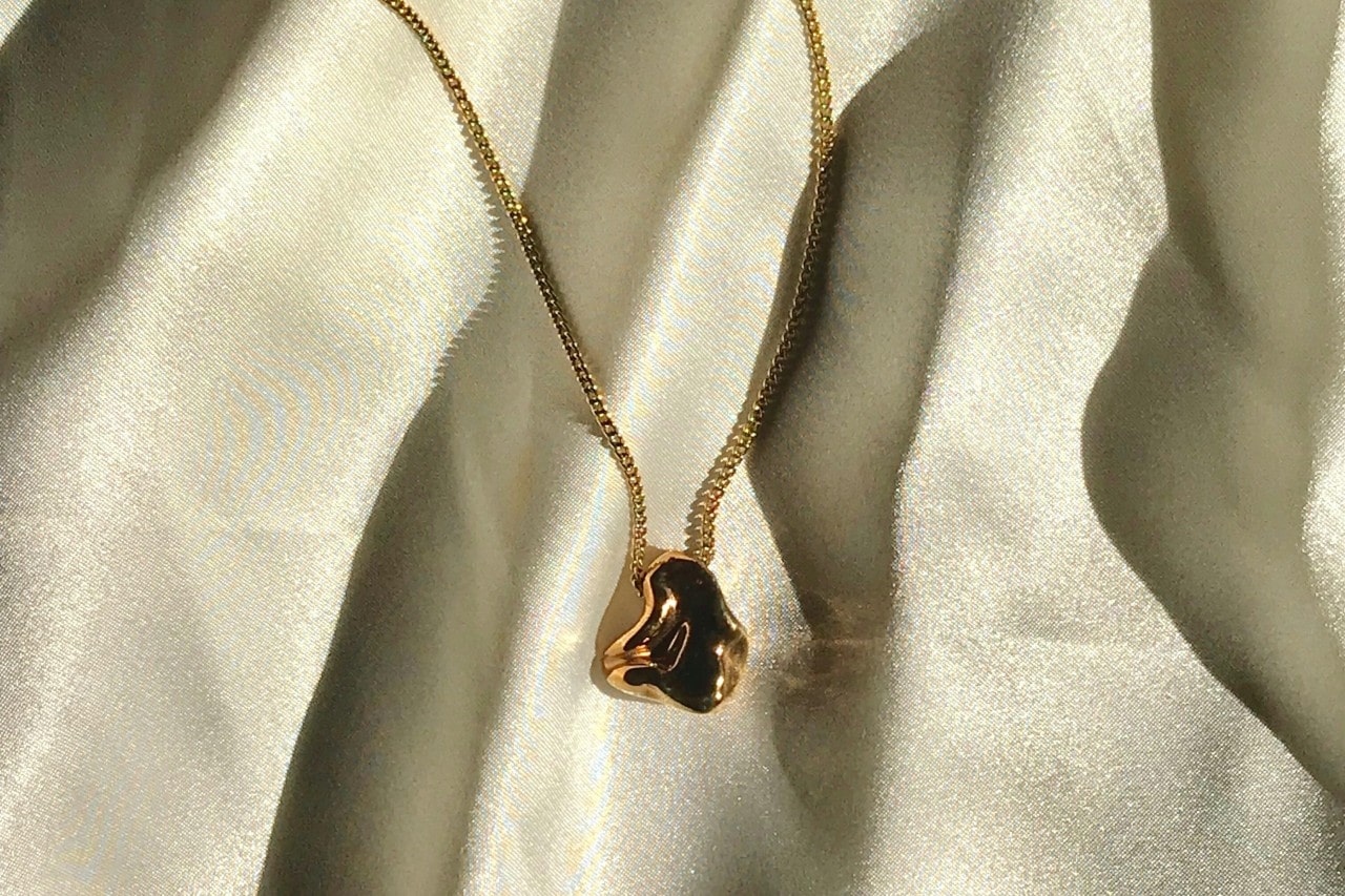 a yellow gold chain necklaces with a sculptural pendant on white fabric