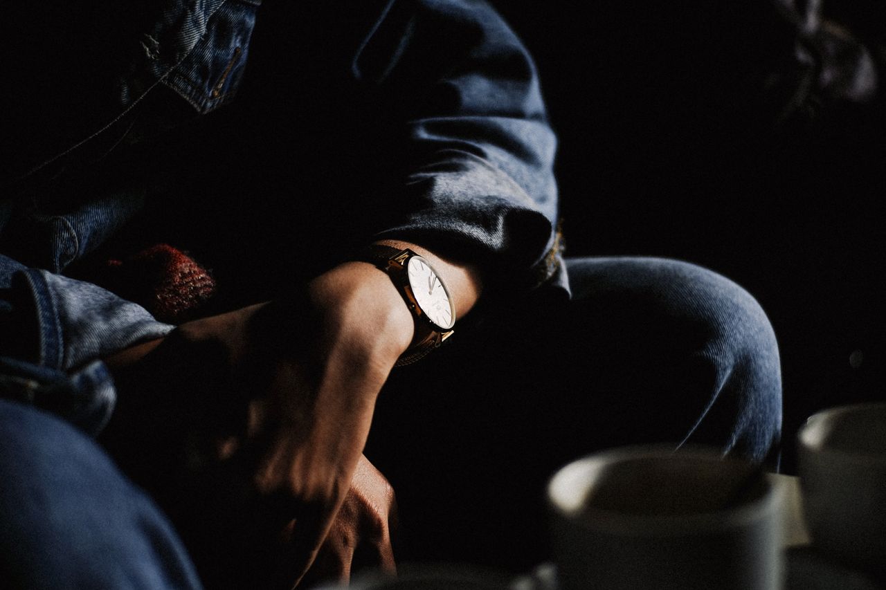 A man leans toward a coffee table with his mug, folding his hands with a watch.