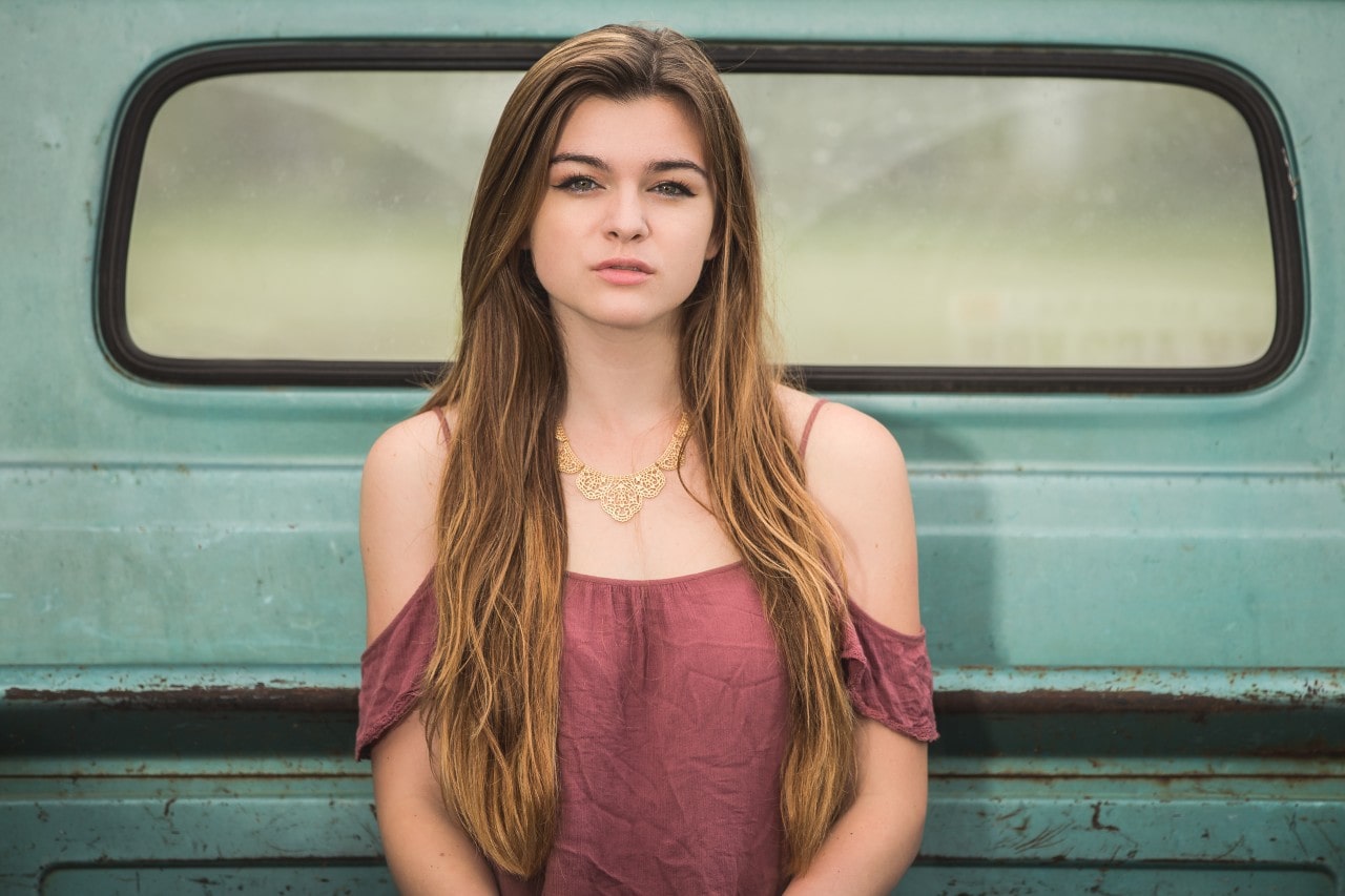 A woman wearing a gold necklace sits in the back of an old turquoise truck.