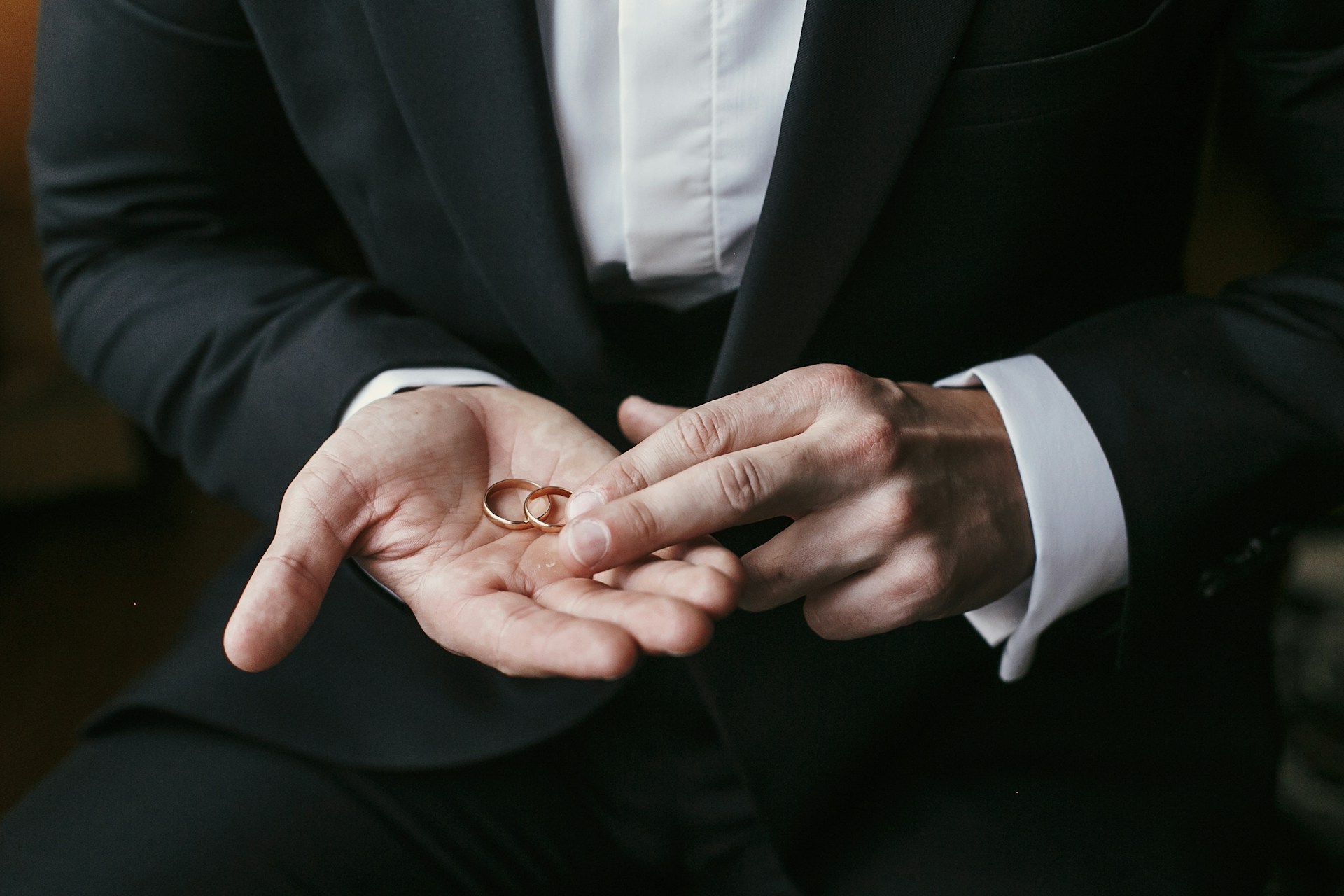 A groom holding matching yellow gold wedding bands in his hand.