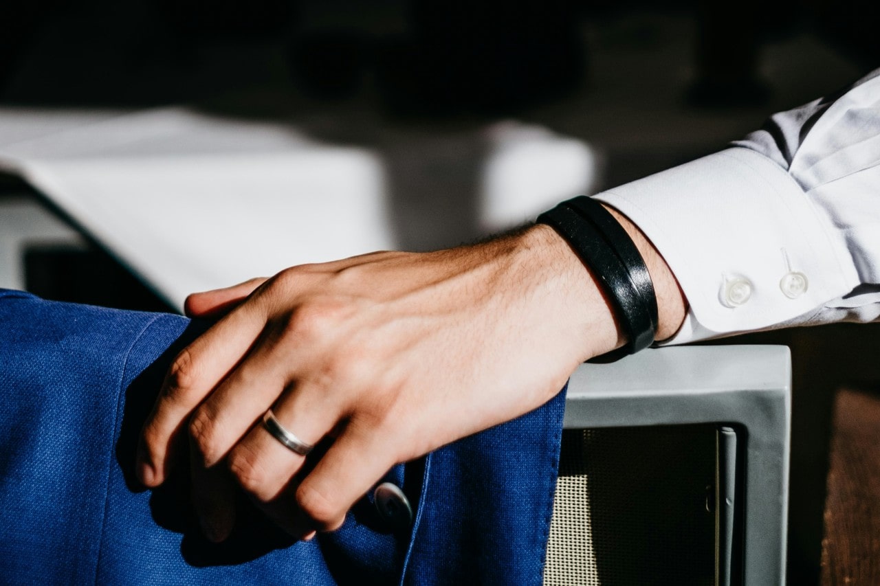 A man’s hand resting on a chair and donning a polished wedding band.