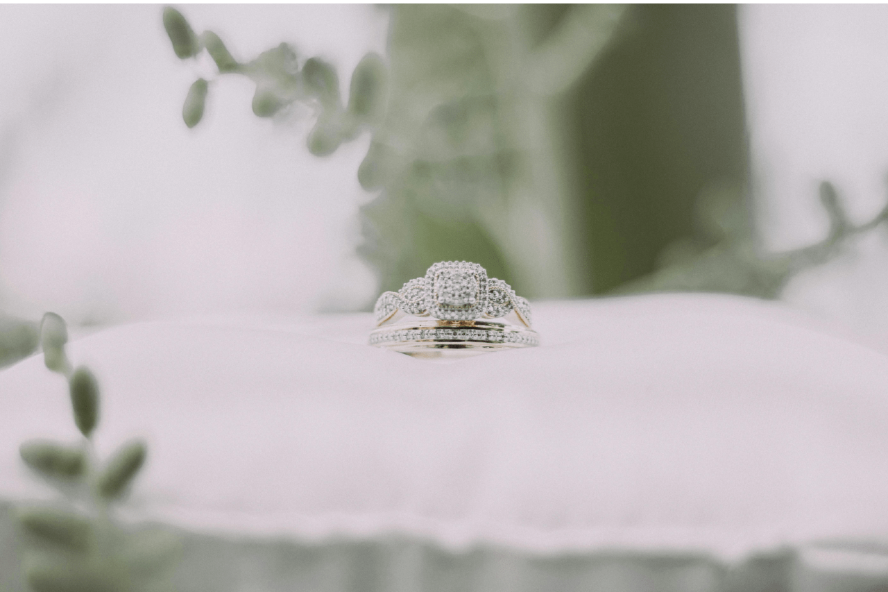 A matching white gold engagement ring and wedding band set lying on a white pillow.