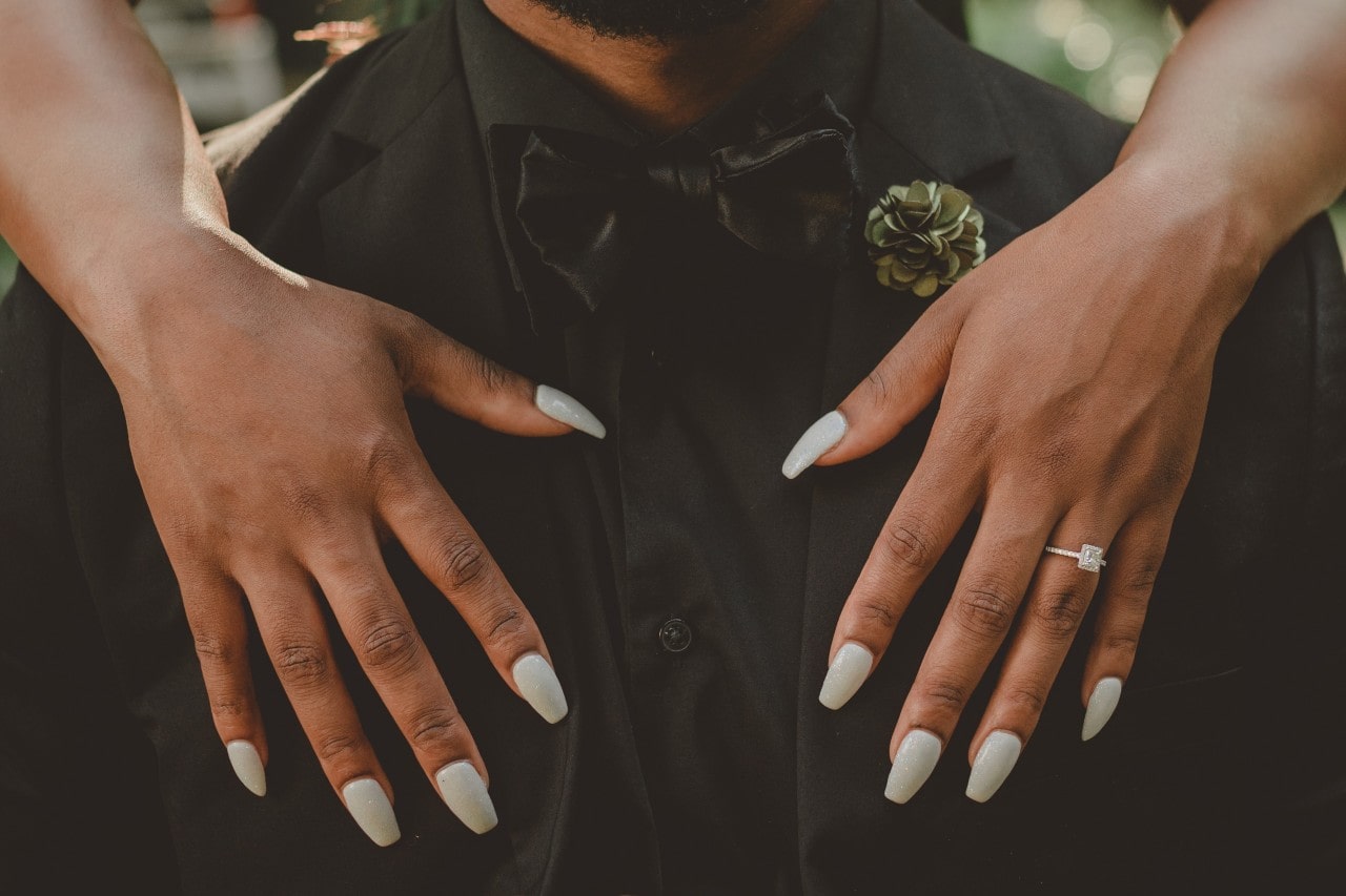 A woman wearing a princess cut diamond engagement ring puts her arms around her husband