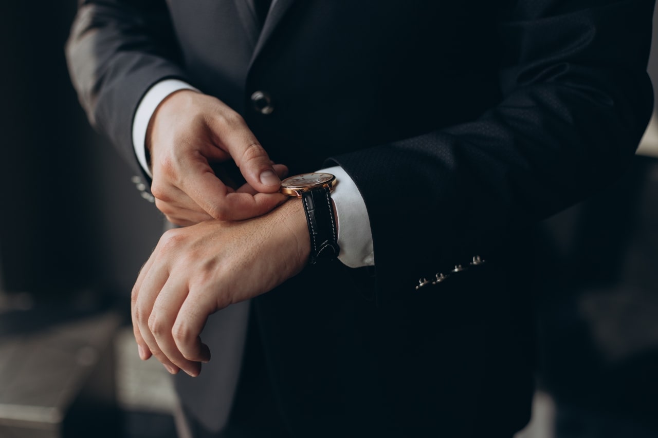 man in suit adjusting time on watch